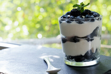 Cottage cheese dessert with blueberries, blackberries and mint in a transparent glass glass. View from the window in the background.