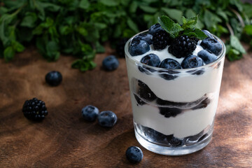 Fototapeta na wymiar Cottage cheese dessert with blueberries, blackberries and mint in a transparent glass glass. On a wooden background. Yummy.