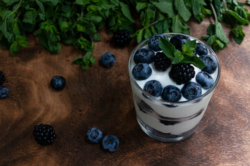 Cottage cheese dessert with blueberries, blackberries and mint in a transparent glass glass. On a wooden background. Yummy.
