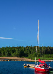 Beautiful red yacht against the blue sky and green forest. It's a great contrast. Good background for a postcard.