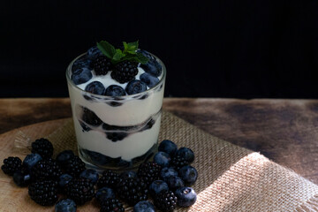 Cottage cheese dessert with blueberries, blackberries and mint in a transparent glass glass. On a burlap napkin and on a wooden background. Delishious.