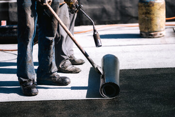 Construction workers, roofers installing rolls of bituminous waterproofing membrane for the...