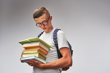 smart student in glasses with a backpack and a stack of books in his hands