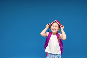 happy, naughty little schoolgirl with a backpack, holding a book on her head