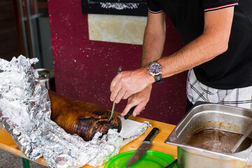 Man cutting roasted pork, with the skin still on it