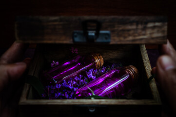 Person opening a wooden box containing glass bottles with purple potions and flowers