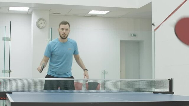 Confident concentrated sportsman playing ping-pong with unrecognizable sportswoman in gym. Portrait of Caucasian man plays table tennis with woman indoors. Workout concept.