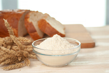 Glass bowl with flour and branches of natural wheat on the light white wooden table and bread pieces