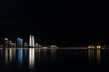Suzhou business center viewed from the lake with colorful lights reflecting in the water.