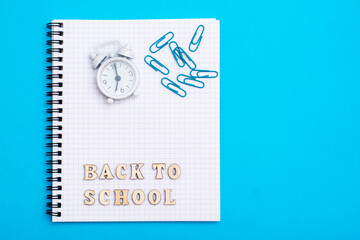 Back to school. Alarm clock, wooden letters and paper clips on a notebook on a blue background