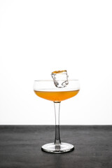 An ice cube falling into a coupe glass with an orange cocktail