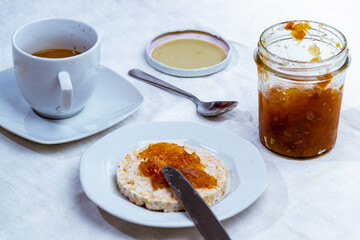 still life con desayuno con taza de cafe y mermelada de peras, con galleta de arroz sobre mantel blanco rustico