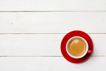High angle view of coffee in red cup with saucer on white wooden background, close up