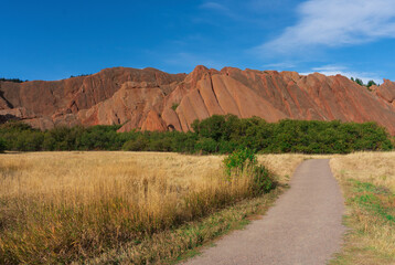 Obraz premium Dirt Walking Path in Park Through Golden Meadow Leading to Red Rock Formations