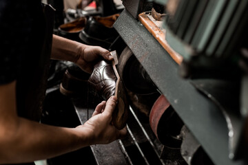 Male shoemaker repairing sole of shoe on grinding machine. Cobbler at work.