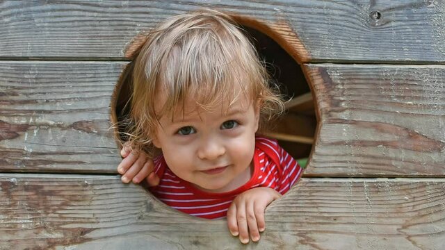 Cute little child having fun inside a wooden house in the park. Beautiful summer sunny day in children playground