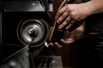 Male shoemaker repairing heel of shoe on grinding machine. Cobbler at work.