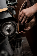 Male shoemaker repairing heel of shoe on grinding machine. Cobbler at work.