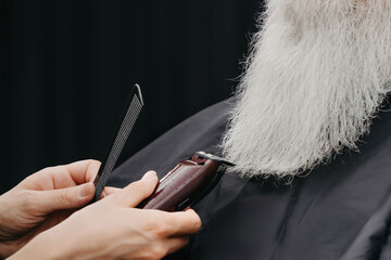 Woman barber cutting beard to an aged bearded man. Elderly man in barbershop concept.