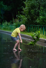Boy in a yellow t-shirt playing with puddles in the rain