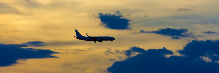 Fototapeta na wymiar Airplane taking off at the sunset sky, silhouette of aircraft in the sky. Wide banner background