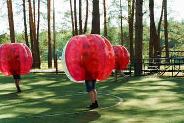 Bubble football sport game. Football players play bumperball on the green field. Team building. Man...