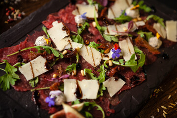 Obraz na płótnie Canvas Beef carpaccio with pepper, rucola and parmesan served on a board. Delicious healthy Italian traditional antipasti snacks food closeup served for lunch with wine in modern gourmet cuisine restaurant