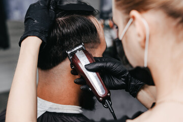 Fototapeta na wymiar Woman barber cutting hair to a bearded man in face mask. Quarantine haircut concept.