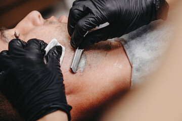 Woman barber shaving a man with a straight razor. - obrazy, fototapety, plakaty