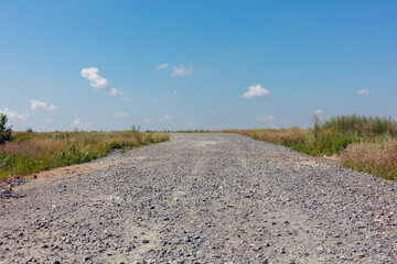 Green grass and farmlands below. A bright, sunny day. Gravel path in the fields under blue sky with...