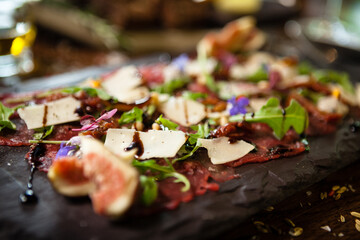 Naklejka na ściany i meble Beef carpaccio with pepper, rucola and parmesan served on a board. Delicious healthy Italian traditional antipasti snacks food closeup served for lunch with wine in modern gourmet cuisine restaurant