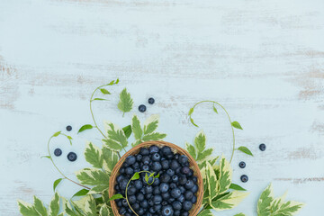 Fresh blueberries in basket with leaves pattern top view. Healthy food on white table mockup. Delicious, sweet, juicy and ripe berry background with copy space for text