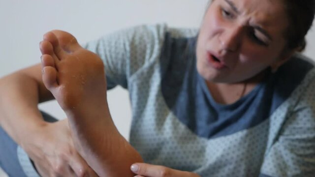 Moisturizing foot mask for dry heels. A woman in a mask on her legs lies on the diva and uses the phone. Self-care during the period of the virus at home