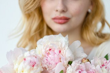 Girl with pink peonies bouquet at white wall