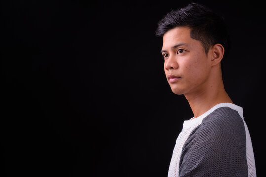 Portrait of young Asian man against black background
