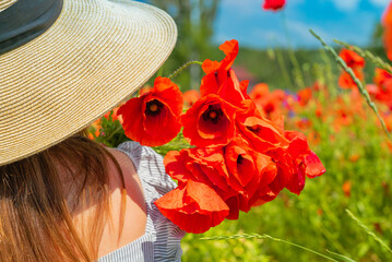 Young girl in the white dress and hat from tha back with a poppy flowers in the hand.
