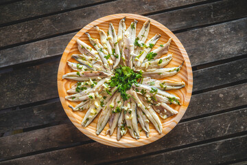 Pickled anchovies with garlic and parsley in a round wooden plate on a dark wooden table. Typical Spanish snack.