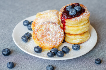 Syrniki or cottage cheese fritters with blueberry jam on a white plate
