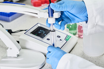 Woman in a rubber gloves holding a glass electrode for measuring of pH of the solution using pH...