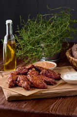 Roasted chicken wings in barbecue sauce and parsley on a wooden board on a table. With copy space. Tasty snack for beer on a dark background