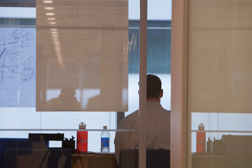 Rear view of businessman sitting at desk seen through glass wall in office