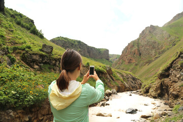 Young woman traveller taking photo in the mountains in Caucasus Russia. Freedom lifestyle.
