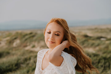 Young asian girl in a white wedding dress in a boho style, in the desert. With red long hair. With beautiful hairstyle and makeup. Makeup with nice false eyelashes. Sea wedding concept. 