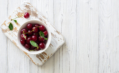 Ripe cherries in white bowl on white wooden background