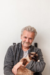 old man hugs a siamese cat on a white background