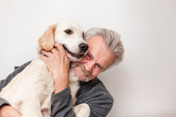 senior man hugs a golden retriever puppy on a white background