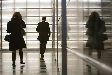 Full length rear view of businesswoman and businessman walking in corridor at office building