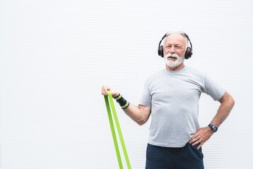 Senior sportsman exercising with resistance band and headphones