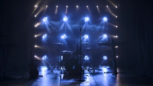 Classic retro chrome microphone and electric guitar together with drums and piano synthesizer keyboard on the stage in dark studio with smoke and neon lighting. Dynamic white neon lighting effects