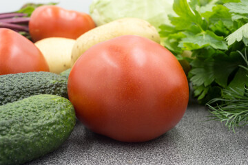 Fresh vegetables on a gray worktop, closeup: Potatoes, green onions, dill, tomato, parsley. Healthy food, vegan food.